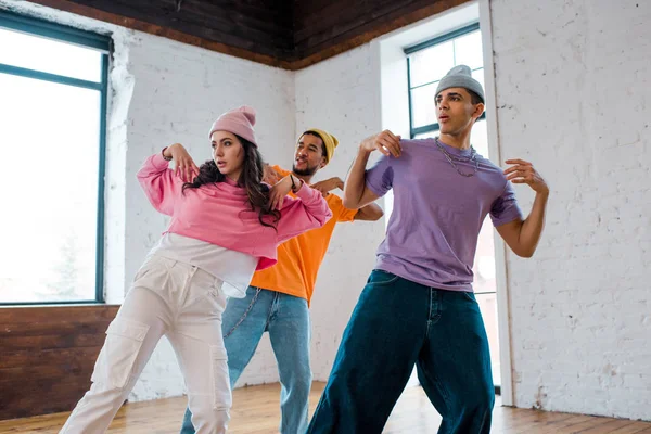 Girl breakdancing and gesturing with stylish multicultural men in hats — Stock Photo