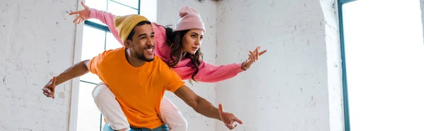 Panoramic shot of attractive girl with outstretched hands breakdancing with african american man in hat — Stock Photo