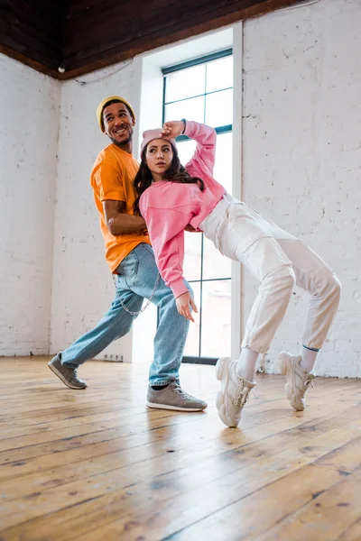 Chica atractiva breakdancing con feliz africano americano hombre en sombrero - foto de stock