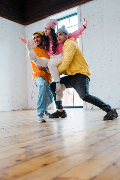 Стильні мультикультурні чоловіки в капелюхах тримають привабливого танцюриста — стокове фото