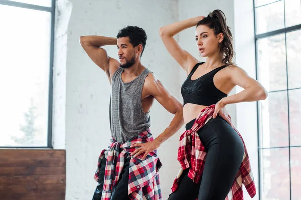 Chica atractiva y guapo afroamericano hombre con las manos en las caderas bailando jazz funk - foto de stock