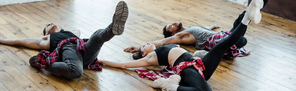 Plano panorámico de hombres multiculturales y mujer atractiva tumbada en el suelo mientras baila jazz funk - foto de stock