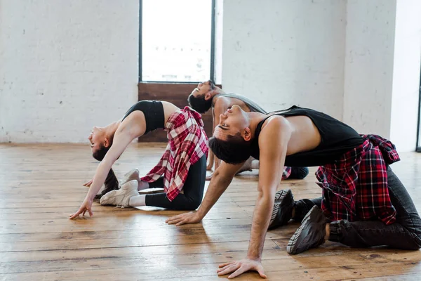 Young woman and multicultural men doing wheel pose while dancing hip-hop — Stock Photo