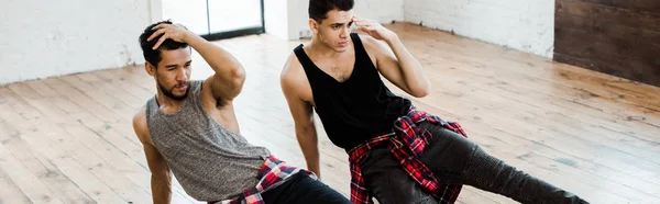 Panoramic shot of handsome multicultural dancers touching hair in dance studio — Stock Photo