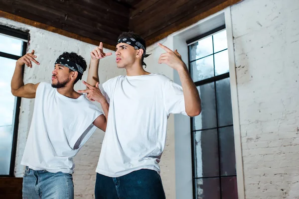Spotlight on handsome multicultural dancers in headbands gesturing in dance studio — Stock Photo