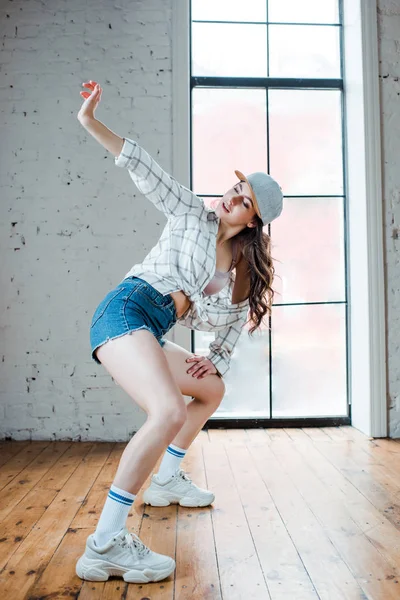 Молодая женщина в джинсовых шортах и кепке танцует хип-хоп — стоковое фото