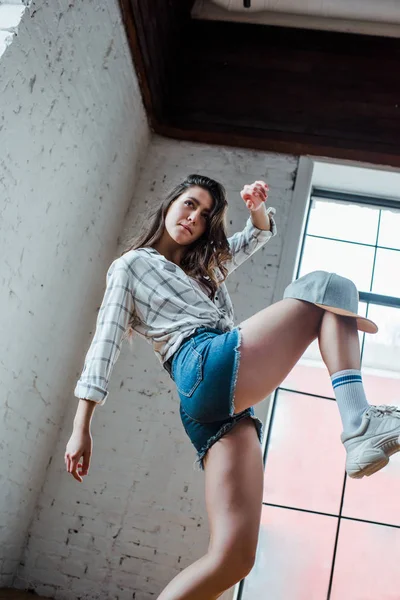 Vista de ángulo bajo de bonita bailarina con gorra bailando hip-hop en estudio de baile - foto de stock