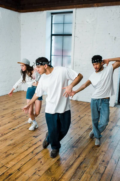 Beaux danseurs multiculturels dans les bandeaux et jolie fille dans la casquette danse hip-hop — Photo de stock