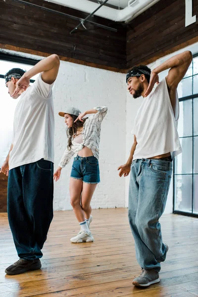 Multicultural dancers in headbands and attractive woman in cap dancing hip-hop — Stock Photo