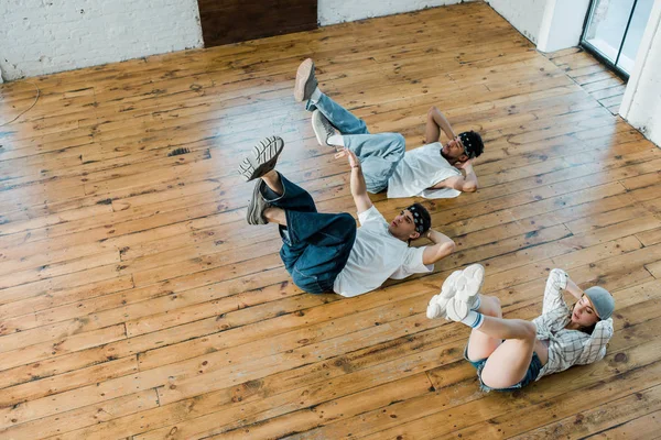 Draufsicht auf trendiges Mädchen, das mit multikulturellen Tänzern auf dem Boden liegt, während Breakdance im Tanzstudio — Stockfoto