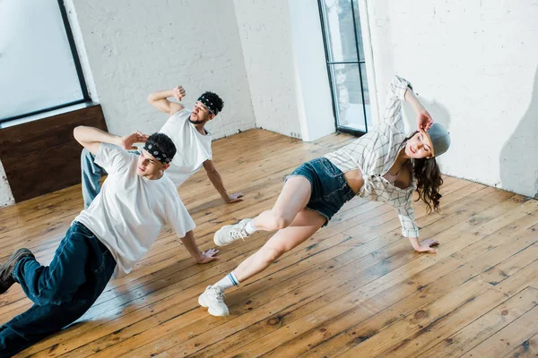 Chica de moda tocando gorra mientras breakdancing con bailarines multiculturales en estudio de baile - foto de stock