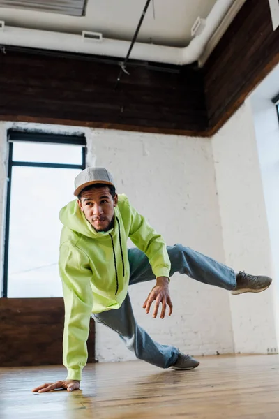 Stylischer und junger afrikanisch-amerikanischer Mann mit Mütze Breakdance im Tanzstudio — Stockfoto