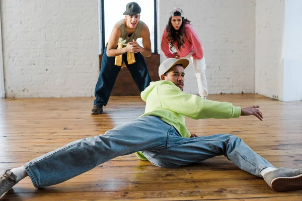 Selective focus of handsome african american man breakdancing near emotional dancers — Stock Photo