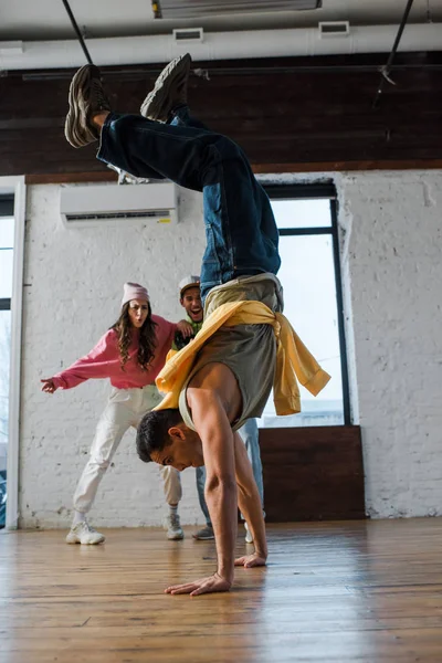 Selective focus of man doing handstand while breakdancing near multicultural dancers — Stock Photo