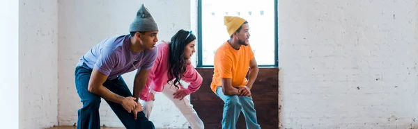 Tiro panorámico de mujer y elegantes hombres multiculturales breakdance - foto de stock