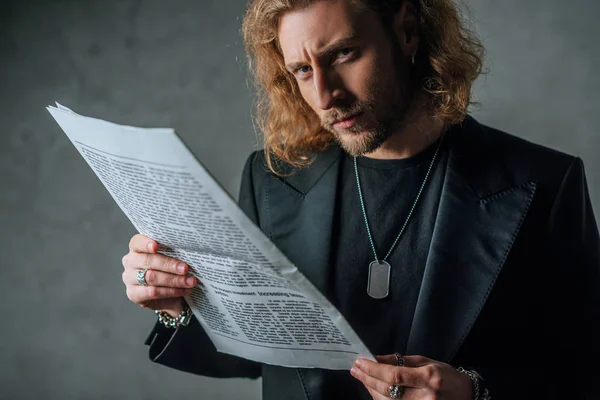 Angespannter modischer Geschäftsmann im schwarzen Anzug, der die Zeitung im Dunkeln hält — Stockfoto