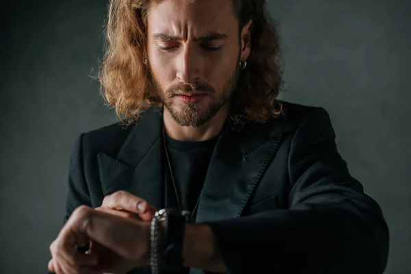 Hombre de negocios de moda en traje negro mirando el reloj de pulsera en la oscuridad - foto de stock