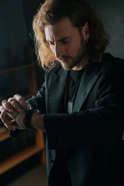 Hombre de negocios de moda en traje negro mirando el reloj de pulsera en la oscuridad - foto de stock
