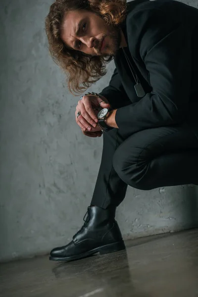 Uomo d'affari alla moda teso in abito nero in posa in parete grigio scuro vicino — Foto stock