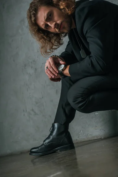 Tenso hombre de negocios de moda en traje negro posando en oscuro cerca de la pared gris - foto de stock