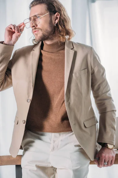 Elegante hombre de negocios de moda de pie cerca del escritorio y mirando hacia otro lado en la oficina — Stock Photo