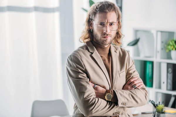 Elegante hombre de negocios de moda posando con los brazos cruzados en la oficina - foto de stock