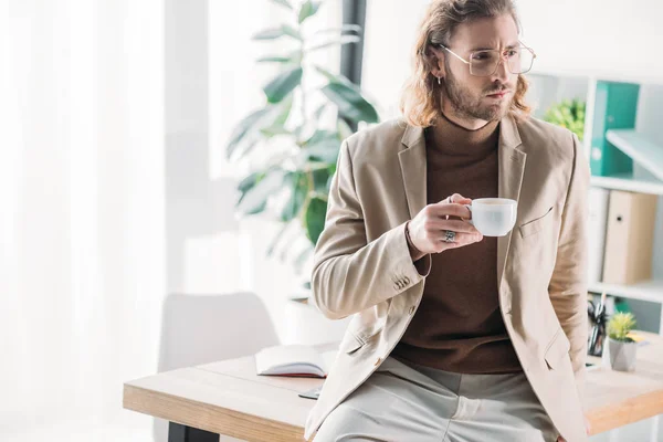 Elegant fashionable businessman drinking coffee in office — Stock Photo
