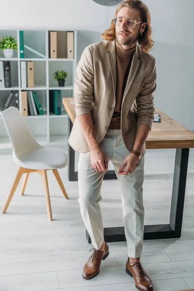 Elegante homem de negócios na moda posando perto da mesa no escritório — Fotografia de Stock