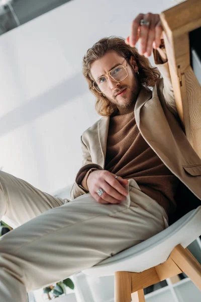 Вибірковий фокус елегантного модного бізнесмена позує на стільці в офісі — стокове фото