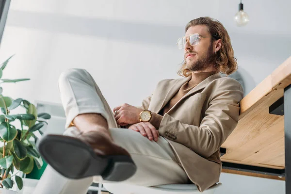 Blick aus dem niedrigen Winkel auf elegante modische Geschäftsmann sitzt auf Stuhl in der Nähe Schreibtisch im Büro — Stockfoto