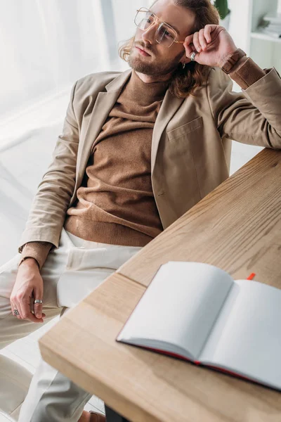 Foco seletivo de homem de negócios elegante sonhador sentado na cadeira perto da mesa com notebook em branco no escritório — Fotografia de Stock
