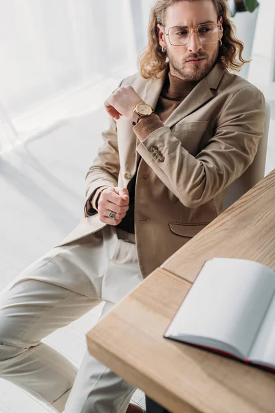 Foco seletivo de homem de negócios na moda pensativo sentado na cadeira perto da mesa com caderno em branco no escritório — Fotografia de Stock