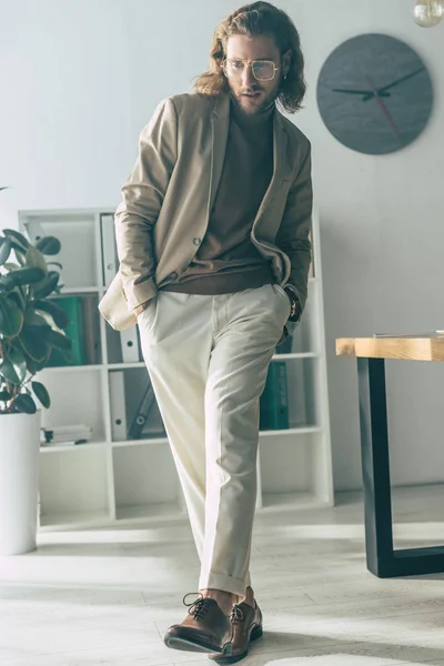 Homem de negócios na moda elegante que anda com mãos em bolsos na luz solar no escritório — Fotografia de Stock