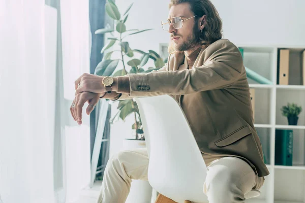 Elegante modische Geschäftsmann posiert auf Stuhl im Sonnenlicht im Büro — Stockfoto