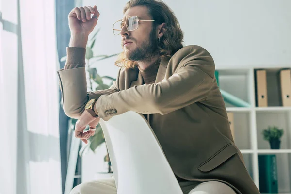 Elegant fashionable businessman posing on chair in sunlight in office — Stock Photo