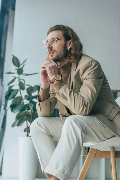 Low-Winkelblick von nachdenklichen eleganten modischen Geschäftsmann posiert auf Stuhl im Büro — Stockfoto