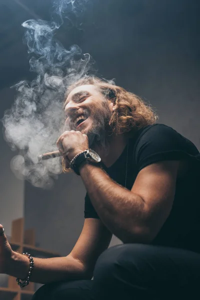 Blick auf einen lächelnden modischen Geschäftsmann im schwarzen Outfit, der Zigarre raucht — Stockfoto