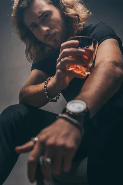 Selective focus of fashionable businessman in black outfit with whiskey near grey wall — Stock Photo