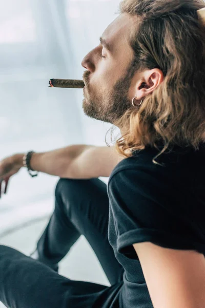 Fashionable casual businessman in total black outfit smoking cigar with closed eyes in office — Stock Photo