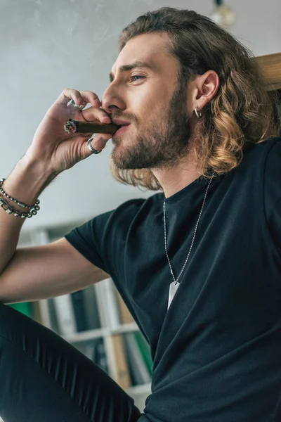 Modischer Gelegenheitsunternehmer im schwarzen Outfit, der im Büro Zigarre raucht — Stockfoto