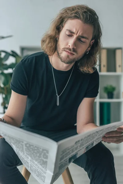 Selective focus of fashionable casual businessman in total black outfit reading business newspaper in office — Stock Photo