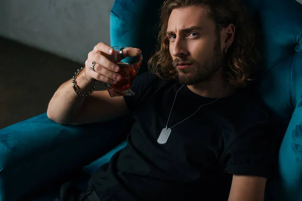 Modeunternehmer im schwarzen Outfit hält Glas Whiskey im Sessel — Stockfoto