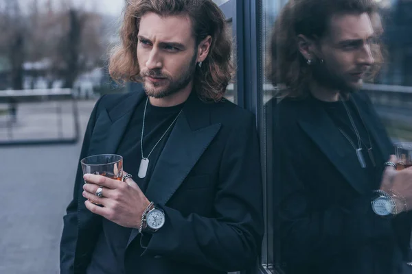 Homme d'affaires à la mode en costume noir tenant un verre de whisky près de l'immeuble de bureaux — Photo de stock