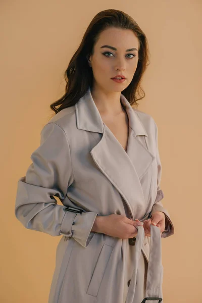 Atractiva joven con abrigo mirando a la cámara aislada en beige - foto de stock