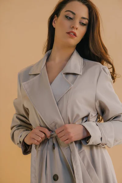 Vista basso angolo di ragazza attraente in cappotto guardando lontano isolato sul beige — Foto stock