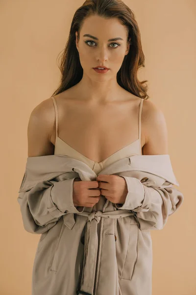 Bella giovane donna in reggiseno e cappotto guardando la fotocamera isolata sul beige — Foto stock