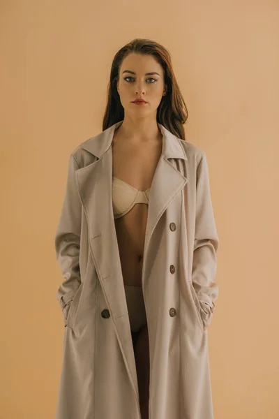 Femme sexy en lingerie et manteau regardant la caméra isolée sur beige — Photo de stock