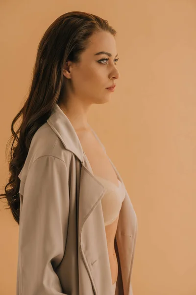 Side view of beautiful girl in coat and bra looking away isolated on beige — Stock Photo