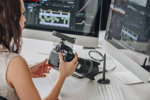 Editor de arte segurando câmera digital perto da mesa com monitores de computador — Fotografia de Stock