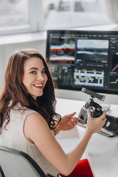 Editor de arte feliz celebración de cámara digital cerca de la mesa con monitores de ordenador - foto de stock